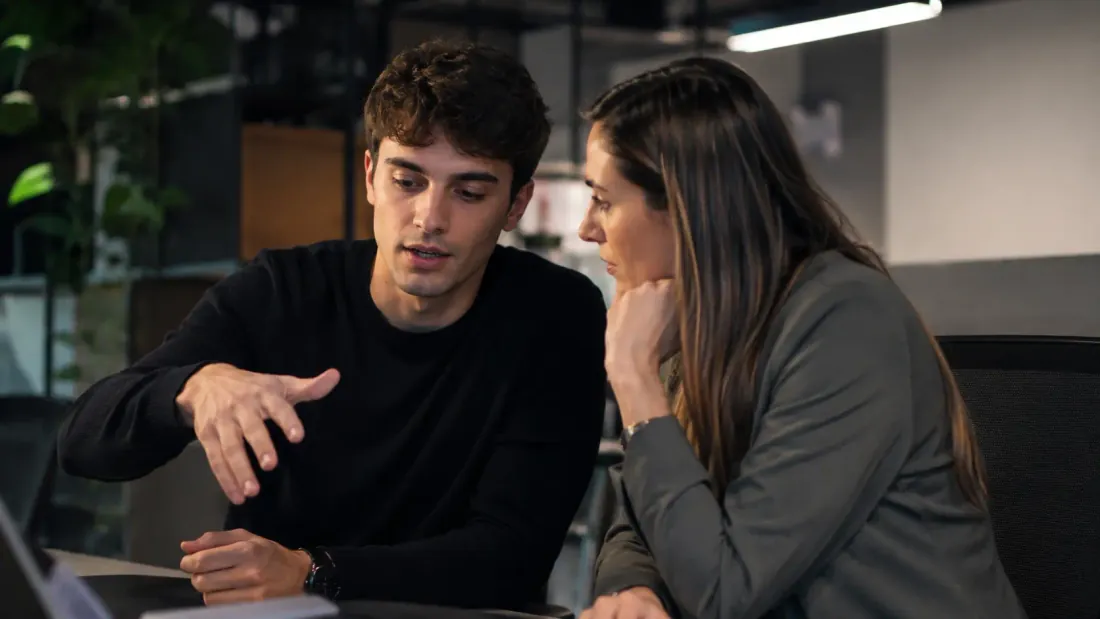 Dos colegas colaborando frente a una laptop en una oficina